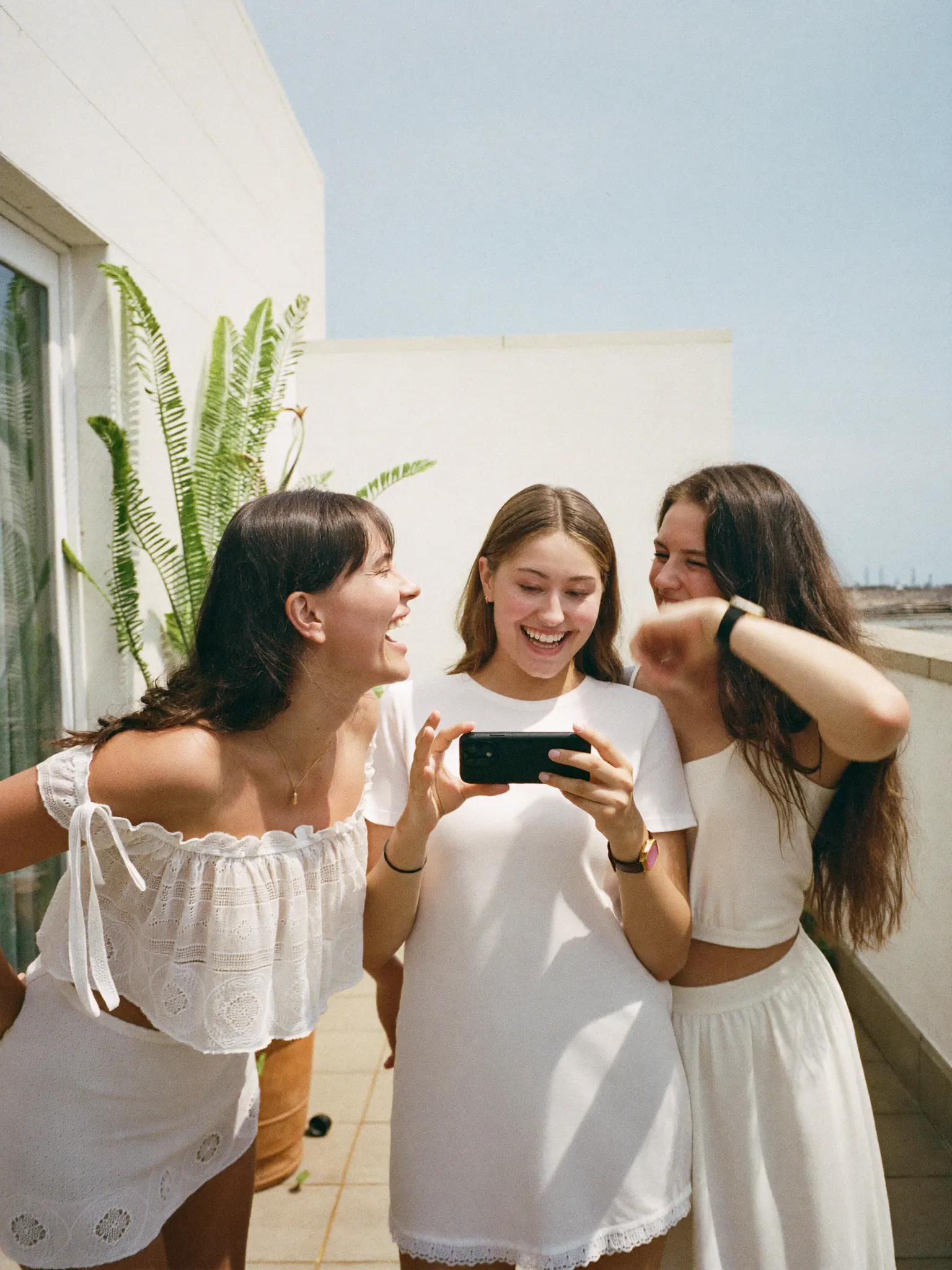 Tres amigas riendo mientras ven un celular en una terraza